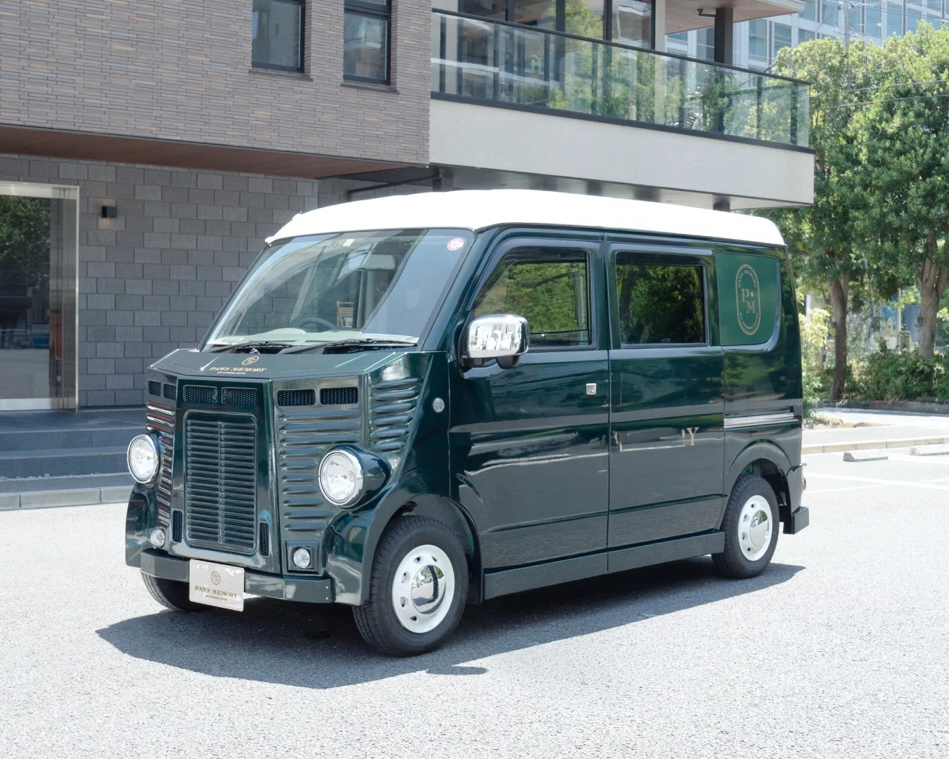 モダンな建物の前に停められた、ダークグリーンと白のツートンカラーのレトロなカスタム軽バン。フロントには「PAWS MEMORY」の文字があり、クラシックな雰囲気を醸し出している。