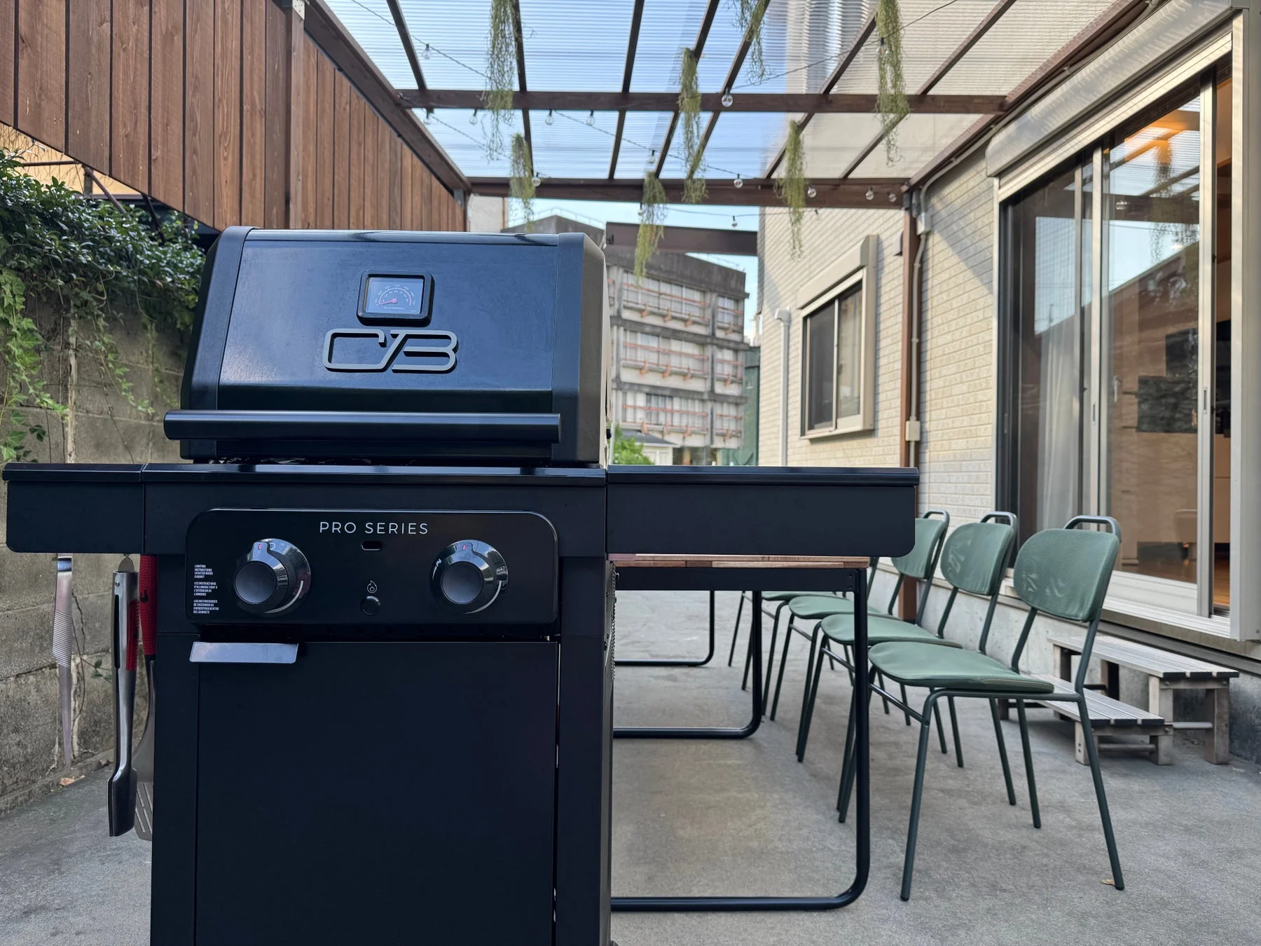 モダンな黒いBBQグリルと屋外用テーブル、緑の椅子が設置されたテラスの風景